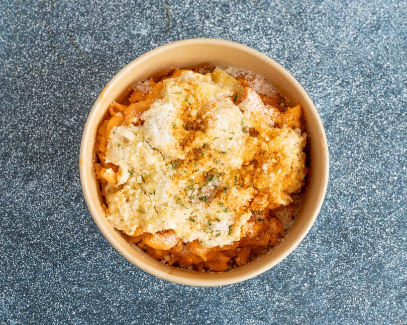 Top-down view of mac and cheese in a brown bowl, topped with breadcrumbs and spices.