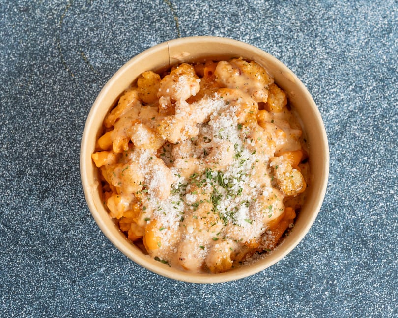 Top-down view of a bowl of mac and cheese topped with crispy shrimp, parmesan, and parsley.